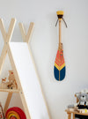 Pagaie décorative en bois munie d'un lacet en cuir décoratif. Fixée à un mur blanc à l'aide d'une attache en cuir de vache huilé.