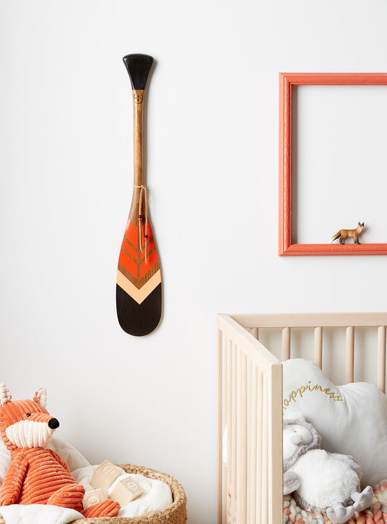 Pagaie décorative en bois L'Étincelle avec lacet fixée sur un mur blanc. 3 couleurs (noir, orange et rose)